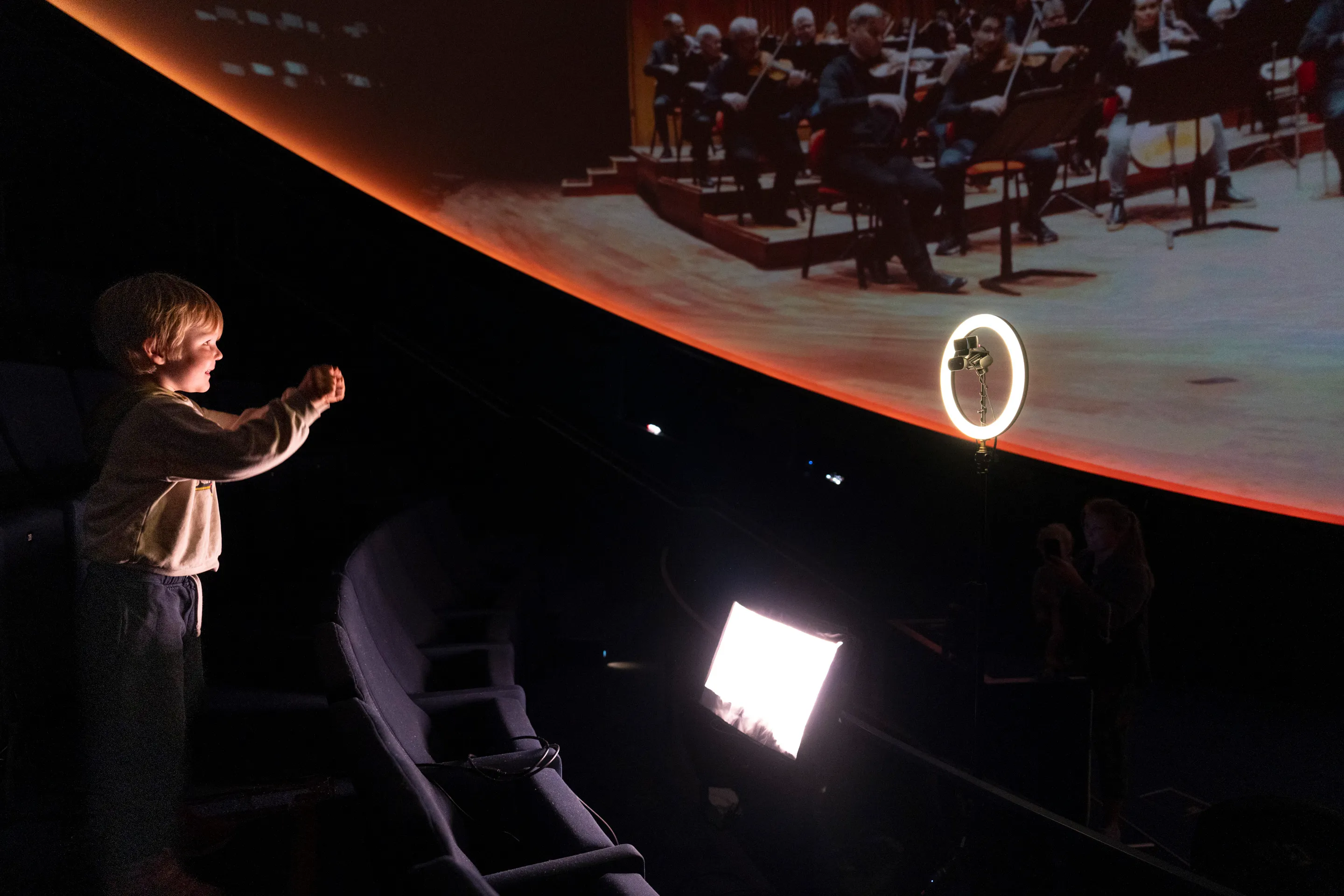 A young visitor takes the podium to conduct the orchestra
